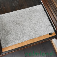 Ward Robe M 尺寸的灰色長絨毛玄關地墊，邊緣飾有棕色仿麂皮飾帶，置於木質地板上。