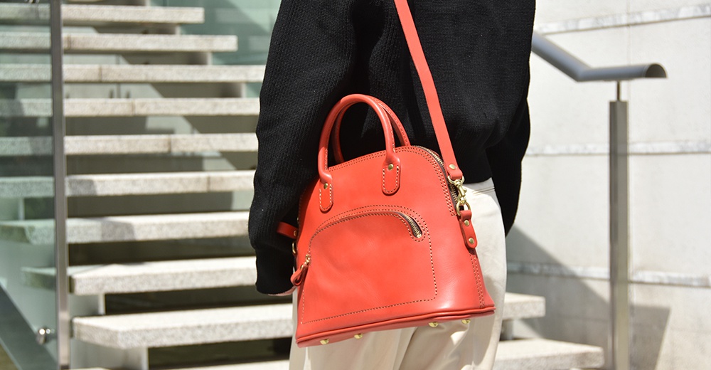 一款亮紅色皮革手提包，經典貝殼造型，帶有頂部提把、可拆卸斜揹帶和一個拉鍊前袋。