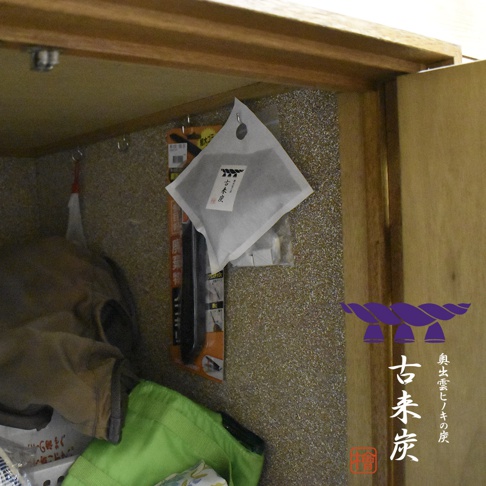 懸掛式方形調濕木炭，白色包裝，內含黑色炭粒，吊掛於衣櫥壁面上，旁邊有衣物及綠色提袋。