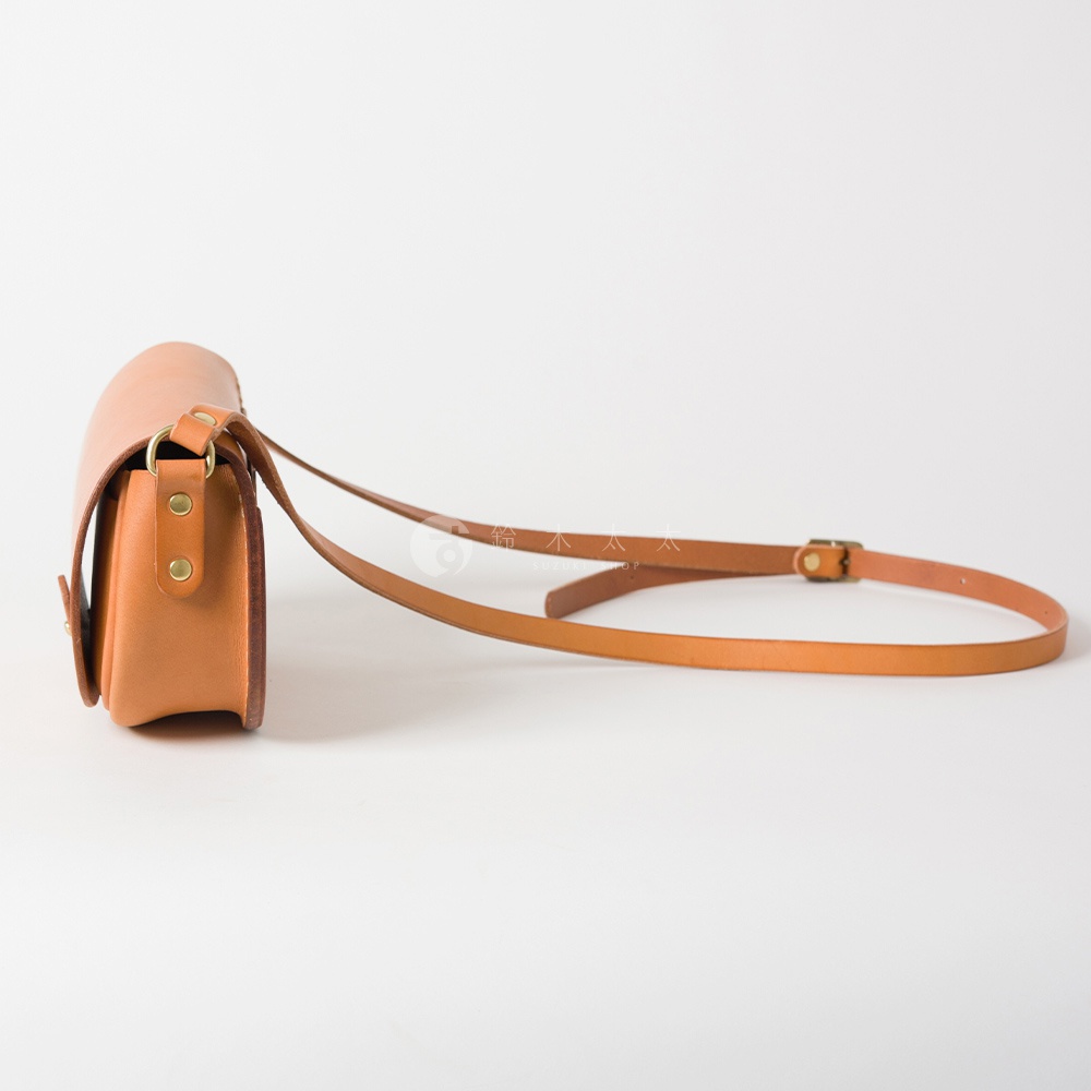 淺棕色皮革迷你馬鞍包，側面視角，附有可調式細長肩帶，搭配金屬扣環。