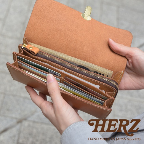 棕色皮革手風琴式長夾，內有多個卡槽，裝有現金和信用卡，搭配金色金屬開合釦，展現職人手作質感。