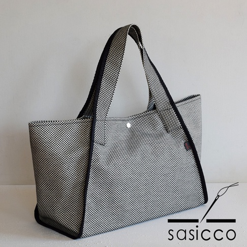 三河木綿刺子織可變形托特包，黑色與白色格紋圖案，配有黑色滾邊和提把，包身側面有品牌標籤。