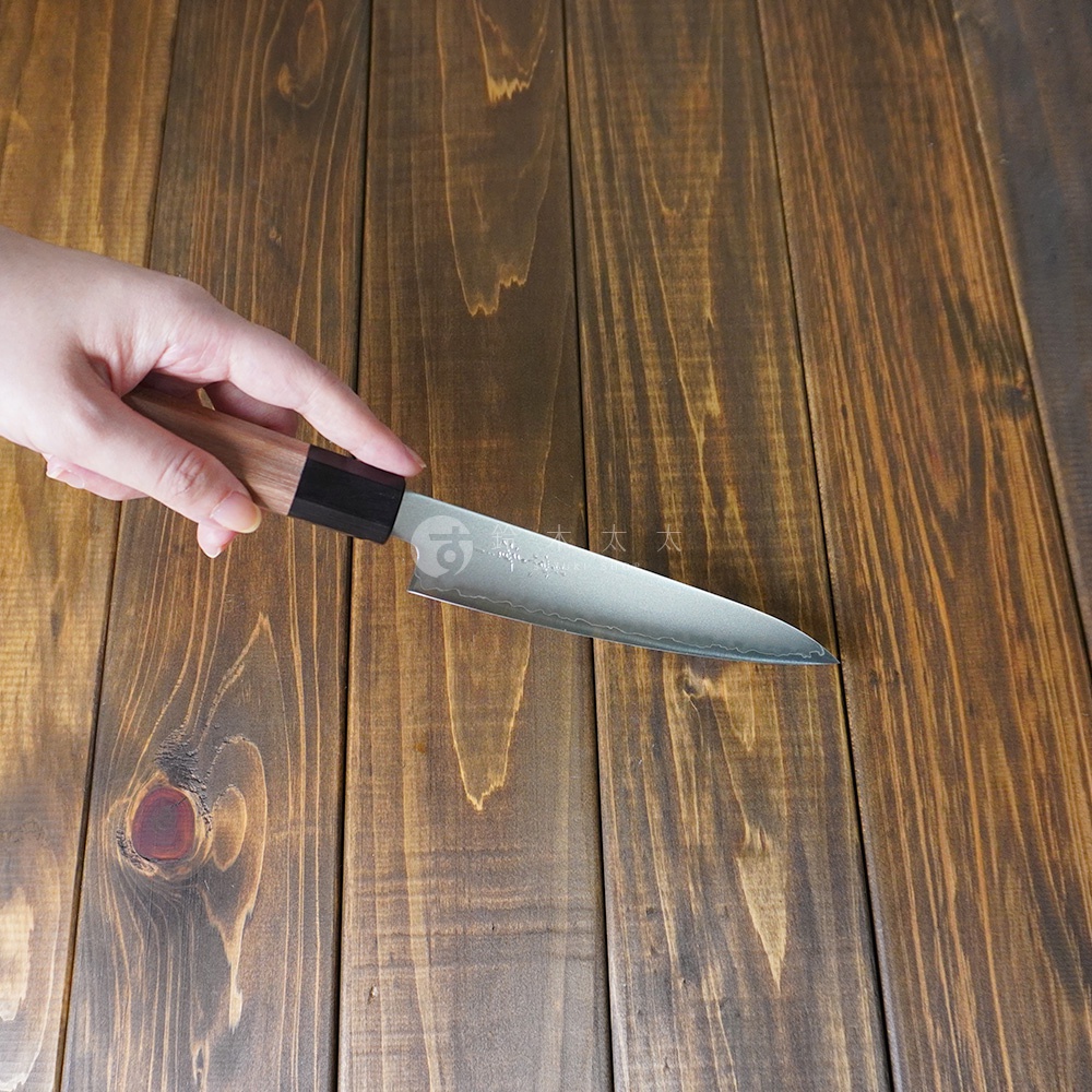 手持一把鋼製水果刀，刀柄為木質，刀身銀色，帶有水波紋路。