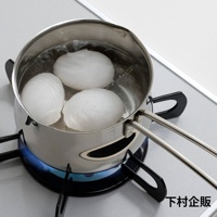 不鏽鋼牛奶鍋內煮著三個白煮蛋，鍋子放在瓦斯爐上，底部有藍色火焰。