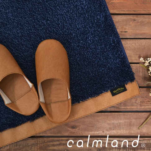 深藍色絨毛廚房地墊，搭配棕色皮革拖鞋，置於木紋地板上，地墊邊緣有「Ward Robe」標籤。