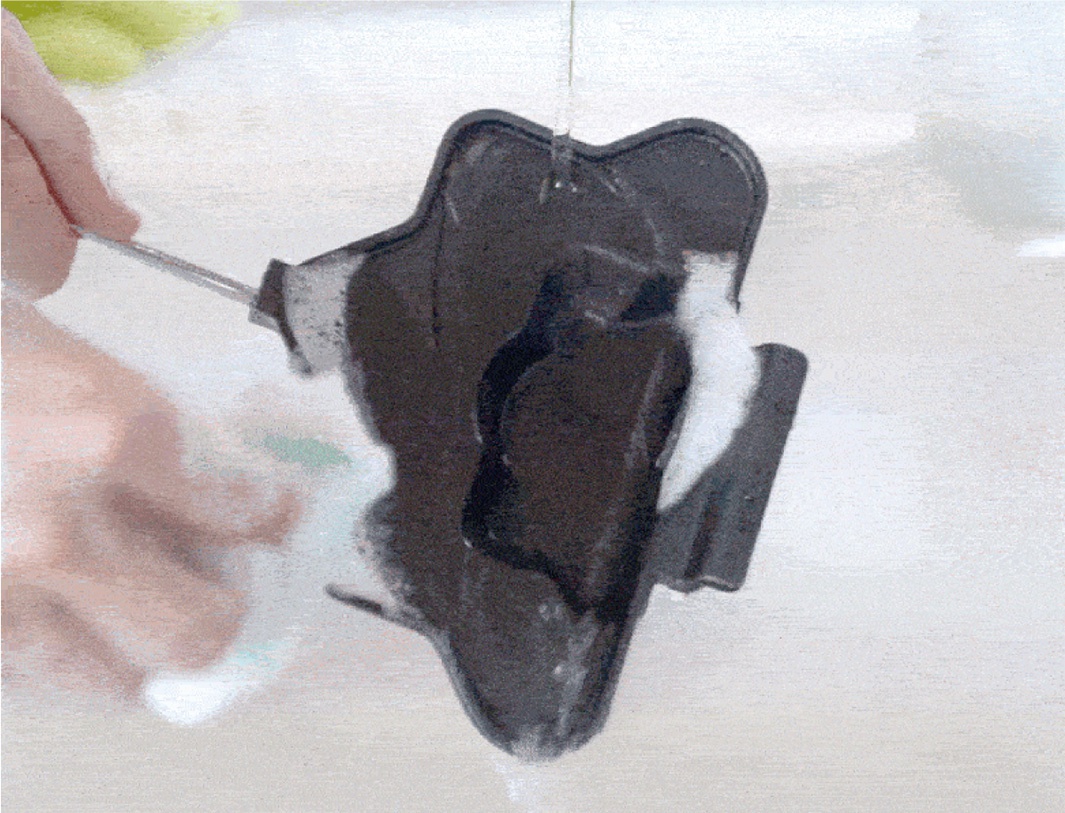 黑色不沾塗層的星型熱壓三明治烤夾，附有金屬手柄，正在被清潔，有泡沫和水流過。