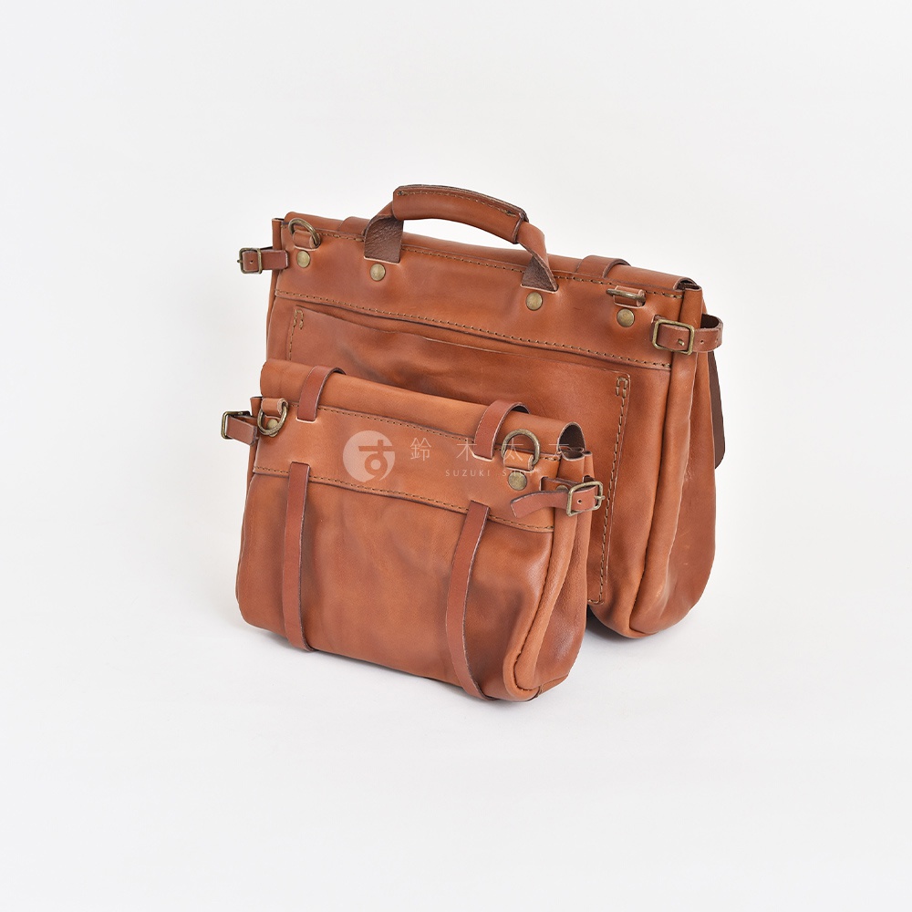兩個棕褐色皮革復古郵差包，一前一後，皆有頂部提把、金屬扣環和皮帶裝飾。