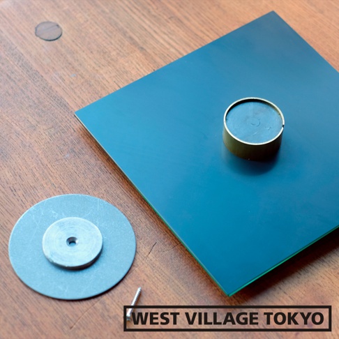 藍色鏡面方形底板，中央帶有金色圓形花器，旁邊有兩個銀色圓形金屬片和一顆螺絲。