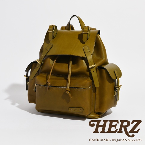 職人手作皮革復古風旅行後背包，橄欖綠色，搭配金色釦環，主體為皮革材質，設有頂部提把、束繩開口、翻蓋、側面口袋及前方拉鍊口袋，設計簡約實用。
