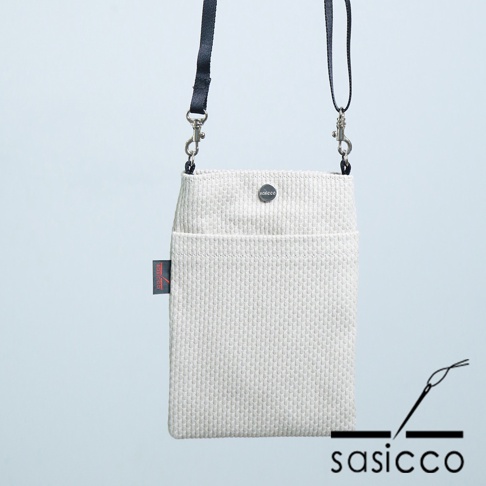 米白色三河木綿刺子織手機包，材質為棉，配有黑色斜揹帶，包身有正面口袋和金屬鈕扣，側面有品牌標籤。