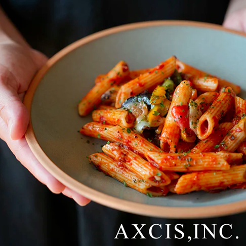 簡約灰綠色陶瓷義大利麵盤，盛裝著淋滿紅色醬汁、搭配烤蔬菜的筆管麵，盤邊呈現自然陶土色調。