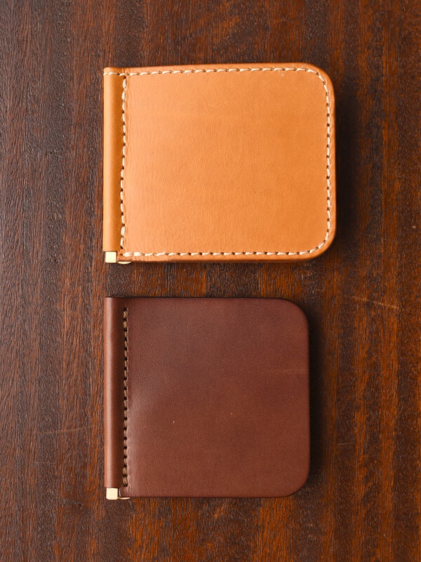 兩款職人手作皮革短夾，一款為淺棕色，另一款為深棕色，皆採橫式對折設計，以白色縫線車邊，並帶有金色金屬夾。