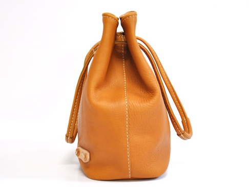 淺棕色皮革束口包，有兩條皮革提把，包身有白色縫線，側面下方有皮革飾釦。