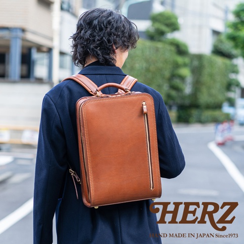 職人手作皮革商務電腦後背包，採用棕色皮革，方形簡約設計，側邊有拉鍊口袋，肩帶和提把皆為皮革材質。