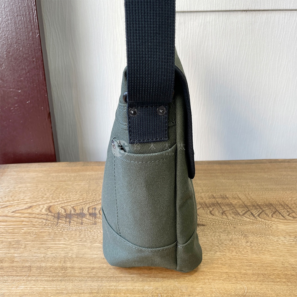 軍綠色純棉帆布雙扣郵差包，側邊視角，顯露其堅固的帆布材質與雙扣設計。