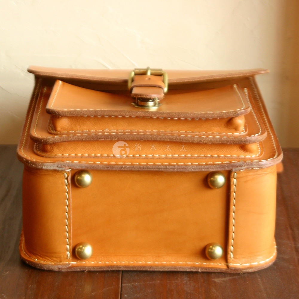 職人手作皮革單肩兩用小方包，淺棕色，設有翻蓋、金屬釦、多層結構及裝飾性金屬鉚釘，縫線清晰。