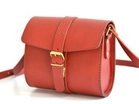 紅色皮革製成的單肩包，包蓋上有皮扣和黃銅搭扣，肩帶亦由皮革製成，縫線明顯。