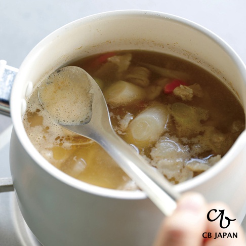 CB JAPAN 日本製不鏽鋼瀝汁匙正在從一鍋湯中撈取湯汁，湯中含有蔬菜塊和肉塊。