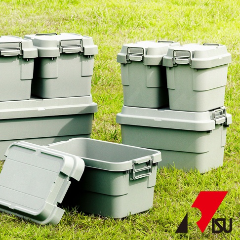 綠色草地上堆疊著數個淺灰色、可堆疊的塑膠收納箱，箱子帶有兩側的扣環和蓋子，其中一個箱子的蓋子打開，露出內部。