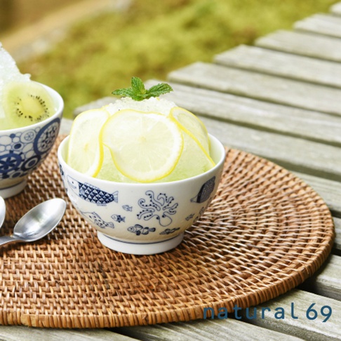 日式飯碗，白色陶瓷，繪有藍色魚、章魚及海洋生物圖案，碗內盛裝刨冰，頂部裝飾檸檬片及薄荷葉，置於藤編墊上。