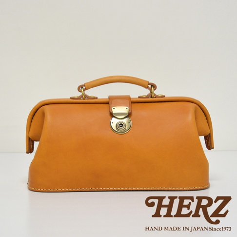 職人手作皮革長型迷你醫生包，採用自然色調皮革製作，配有金色圓形旋轉鎖扣及皮革提把，包身線條流暢，結構紮實，展現復古質感。