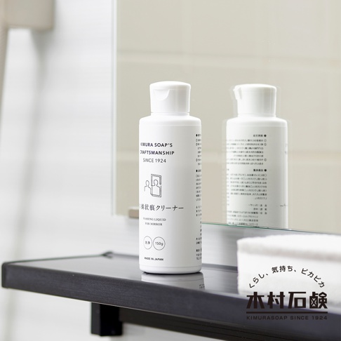 白色塑膠瓶裝的 C-series 鏡面水垢清潔劑，瓶身印有黑色文字與圖案，標示「KIMURA SOAP'S CRAFTSMANSHIP SINCE 1924」、「鏡狀水垢清潔劑」及「WASHING LIQUID FOR MIRROR」，另有 150g 的容量標示與「MADE IN JAPAN」字樣。產品放在黑色檯面上，映照在後方的鏡子中。