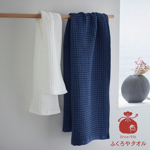 兩條紋理浴巾，一條白色，一條深藍色，掛在木棍上。