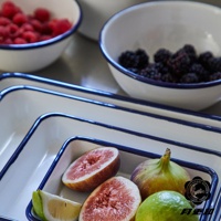 白色琺瑯調理盤，配有深藍色滾邊，盤內盛有切開的無花果、青檸和一碗覆盆子。