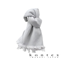 一件淺灰色、微透、輕柔的羊毛棉質混紡絲巾，頂部打結，垂墜感良好，底部有流蘇細節。