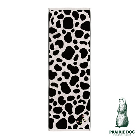 一條長條形的白色毛巾，表面布滿黑色不規則的斑點圖案，右下角處藏著一隻細緻的黑白配色貓咪刺繡，呈現出貓咪從斑點中探出頭來的可愛模樣。圖片右下方印有綠色的草原犬鼠圖示與 Prairie Dog 的品牌文字。