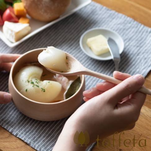 一隻木製湯匙舀起湯碗中的白色塊狀物，湯碗邊緣有綠色香料點綴。