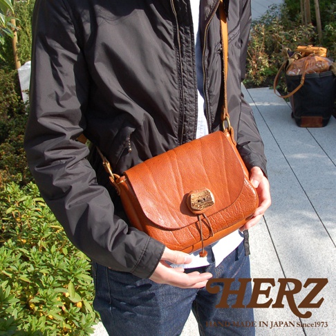 焦糖色皮革肩背包，帶有鹿角形狀的扣環和抽繩設計，皮革表面有自然的紋理。