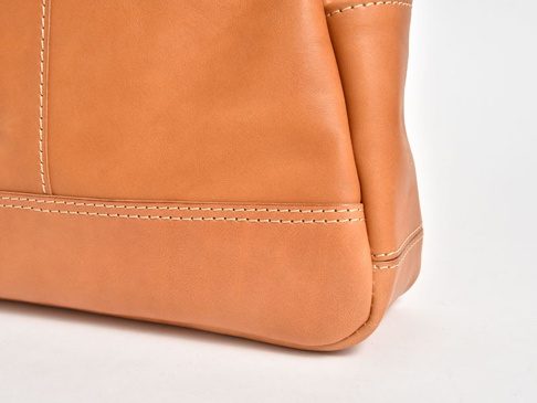 一側特寫職人手作皮革直式肩背托特包，採用天然棕褐色皮革，縫線清晰，質感細膩。