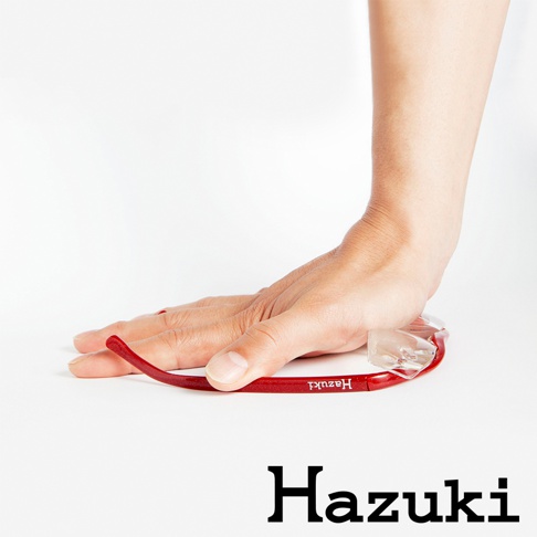 一只手壓在一個紅色的葉月抗藍光放大鏡上，鏡架上有「Hazuki」字樣，鏡片為透明。