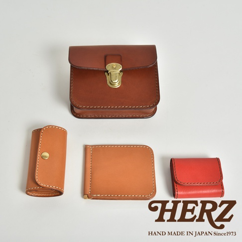 棕色皮革方形腰包，附黃銅鎖扣。左側為捲起式卡夾，右側為紅色皮革零錢包和卡夾。