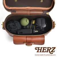 日本HERZ職人手作皮革厚實相機包 N-8，打開的棕色皮革包內裝有綠色鏡頭蓋、Nikon相機及黑色收納袋，下方有HERZ品牌標誌及 HAND MADE IN JAPAN Since1973 字樣。
