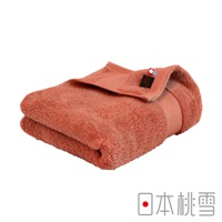 一條珊瑚色今治匹馬棉浴巾，質地柔軟，邊緣處有黑色品牌標籤和紅藍條紋裝飾。