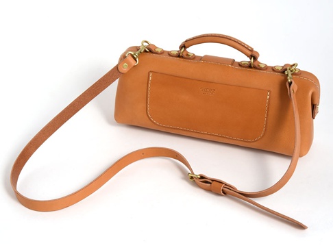 職人手作皮革橫長形單肩包，採用鞣製皮革製成，經典的醫生包造型，配有可調節的長肩帶，正面有品牌壓印和貼袋設計，整體為自然的棕褐色。