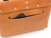 棕褐色皮革後背包，正面有一個可放置手機的 открытый 口袋，縫線清晰，並有金屬鉚釘裝飾。