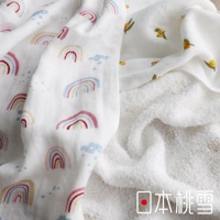 一面印有彩虹圖案的白色紗布方巾，旁邊疊著一條觸感蓬鬆的白色毛巾，毛巾上有著小黃花的圖案，右下角有「日本桃雪」的文字標記。