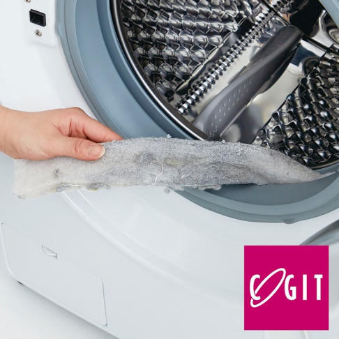 手持一條灰色、帶有絨毛和污垢的滾筒洗衣機門縫清潔條，放置於白色洗衣機的灰色橡膠門封處。