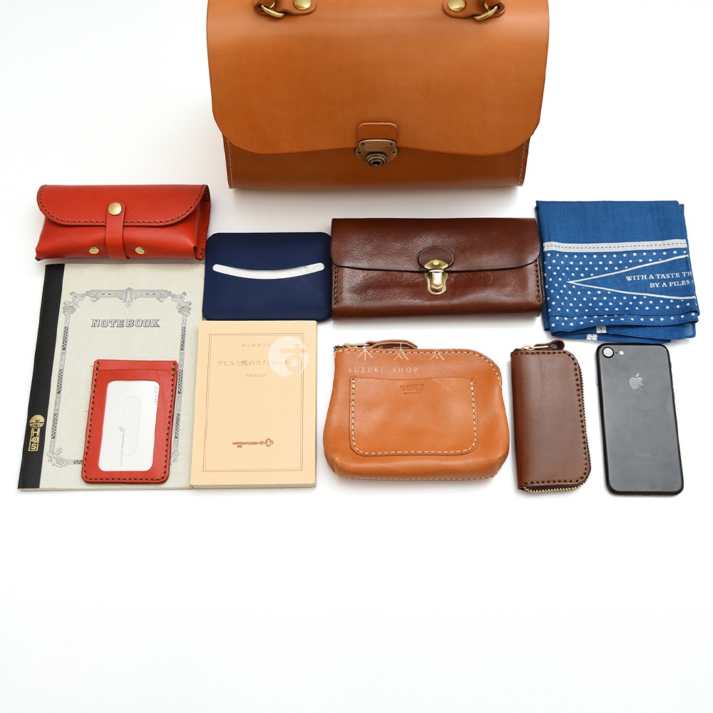 各式皮革收納配件，包含一個棕色大包、紅色皮夾、藍色小包、咖啡色長夾、名片夾、手機、筆記本和一本小書，皆擺放在白色背景上。