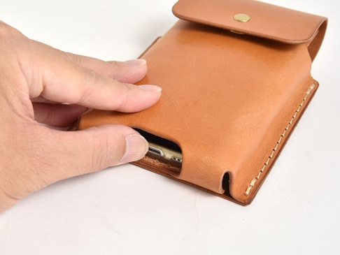 淺棕色皮革製成的手機收納包，頂部有金屬釦，側面縫線整齊，展示手機置入的樣貌。