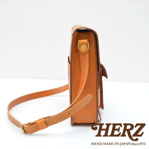 經典厚實的棕色皮革單肩包，側面視角，可見金屬扣環和肩帶。