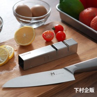 ESSYO 越匠系列可拆式不鏽鋼雙滾輪磨刀器，銀色不鏽鋼材質，設有「1. Diamond」和「2. Ceramic」兩段式磨刀槽。背景有檸檬、小番茄、雞蛋和刀具。