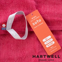 一條桃紅色的毛巾，上面有品牌標籤和吊牌，吊牌上寫有日文和英文的產品資訊。