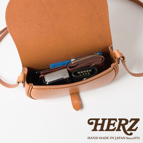 職人手作皮革迷你馬鞍包 CP-8，棕褐色皮革，包內裝有錢包、鑰匙包和銀色長方形物品，展示包的容量與收納功能。