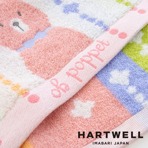 這是一條 HARTWELL 今治森林動物刺繡手帕的特寫鏡頭，手帕呈現溫柔的粉色調，印有可愛的粉色熊圖案及 poppet 字樣，表面採用柔軟的毛巾布材質，邊緣細節細緻，展現日本今治毛巾的高品質質感。