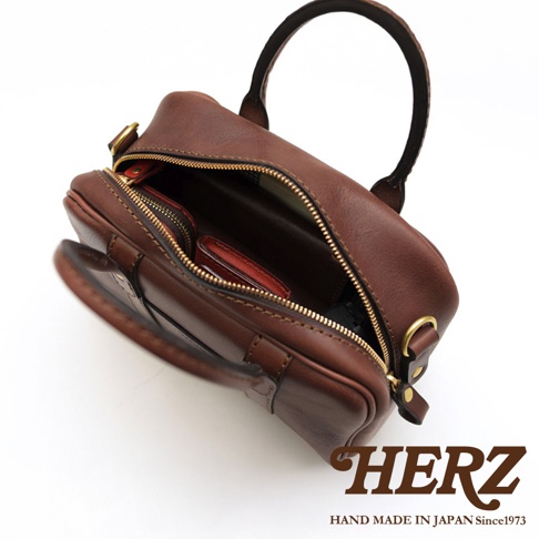 HERZ 職人手作皮革兩用迷你波士頓包，深棕色牛皮革材質，圓潤包身設計，拉鍊開口，內有小皮夾，手提握把，下方有品牌標誌，標示 HAND MADE IN JAPAN Since1973