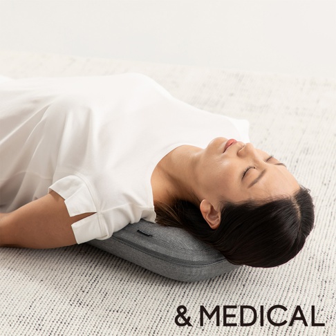 一位女性仰躺在灰色布質按摩指壓枕上，枕頭位於其肩頸下方，枕頭表面有拉鍊。